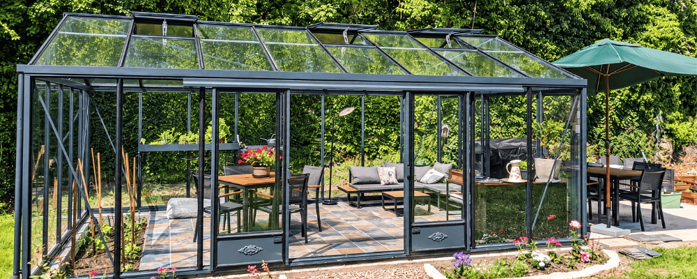 Serre Supra LAMS de 3,80 × 6,04 m aménagée avec une table, des assises et des plantes pour la détente.